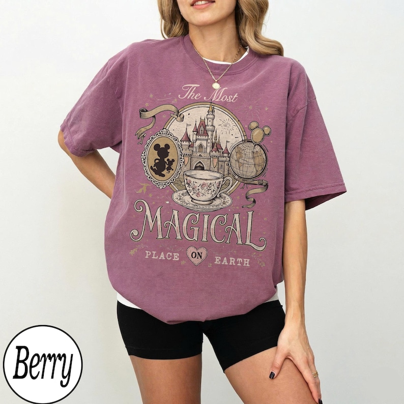May include: Berry-colored t-shirt with a graphic design featuring a castle, teacup, and Mickey Mouse. The text on the shirt reads "The Most Magical Place on Earth."