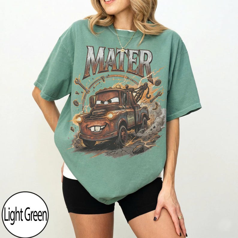 May include: Light green t-shirt featuring a graphic of Mater from the movie Cars. The word "MATER" is printed across the top. The cartoon tow truck is brown with a smiling face and is surrounded by tools and lightning bolts.