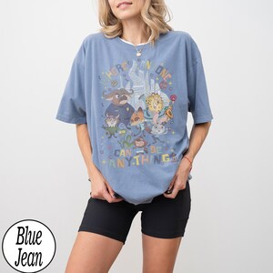 May include: Light blue t-shirt with a cartoon graphic and the words "Where Anyone Can Be Anything." The design features various cartoon characters. The shirt has a relaxed fit.