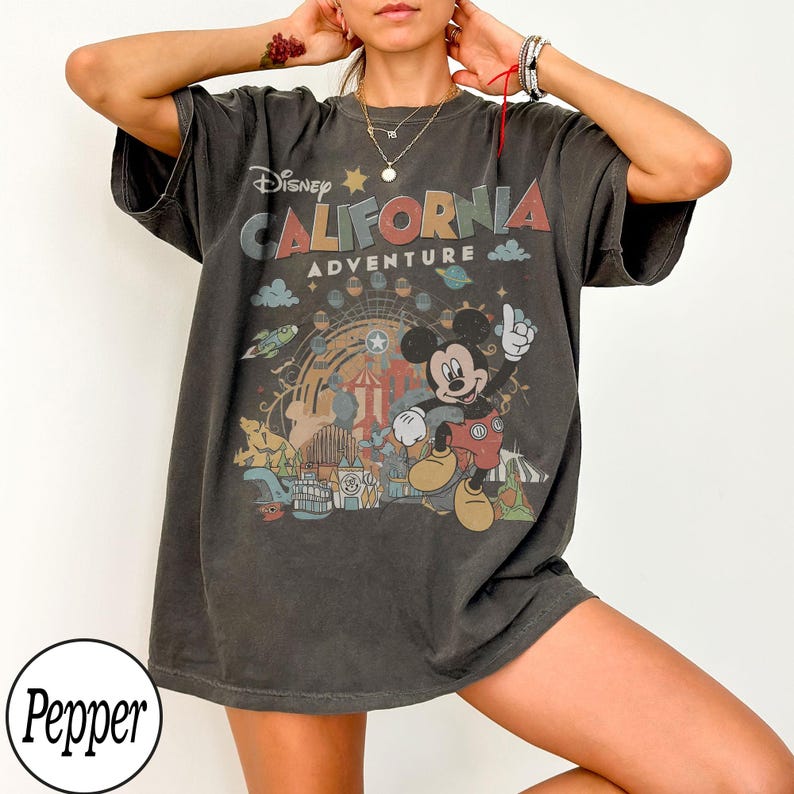 May include: Dark gray t-shirt featuring a colorful graphic of Mickey Mouse in front of a Ferris wheel and the words "Disney California Adventure". The shirt has short sleeves and a relaxed fit, perfect for casual wear.