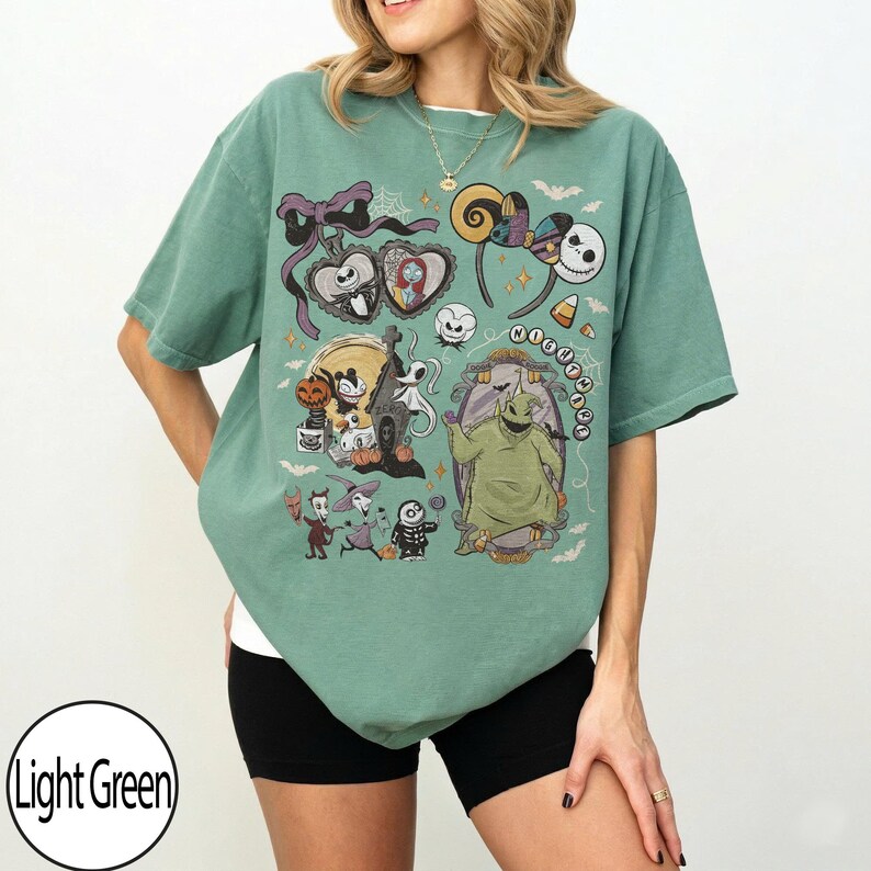 May include: Light green t-shirt featuring a colorful graphic of characters from a popular animated movie. The design includes Jack Skellington, Sally, and Oogie Boogie. The shirt is a relaxed fit and has short sleeves.