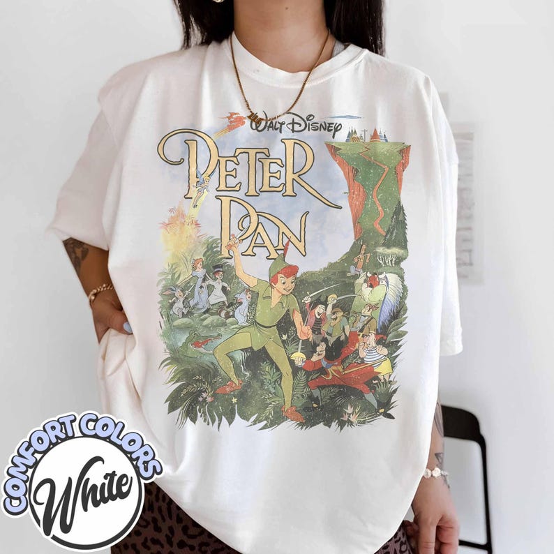 May include: White t-shirt featuring a vintage-style graphic of Peter Pan. The design includes the text "Walt Disney Peter Pan" with illustrations of Peter Pan, Captain Hook, and other characters from the movie. The shirt has a Comfort Colors label.
