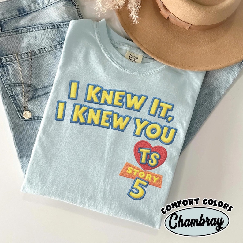 Puede incluir: Una camiseta de manga corta de color azul claro con texto bordado en amarillo que dice I KNEW IT, I KNEW YOU. Debajo del texto hay un coraz&oacute;n rojo con las letras TS, con la palabra STORY y el n&uacute;mero 5 impresos en amarillo debajo.