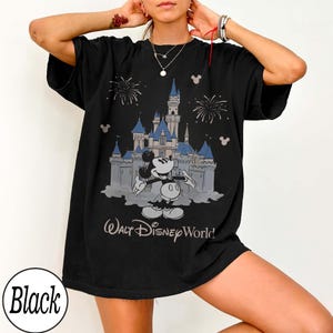 May include: Black t-shirt with a graphic of Mickey Mouse and a castle with blue turrets, and the text "Walt Disney World." The design includes fireworks and Mickey Mouse silhouettes. The shirt is oversized.