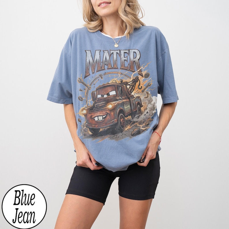 May include: Blue t-shirt featuring a cartoon image of Mater from the movie Cars, with the word "MATER" above the image. The graphic includes a tow truck design with tools and a circular background. The shirt has short sleeves and a round neckline.