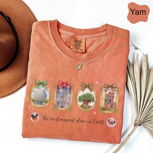 K&ouml;nnte beinhalten: Ein yam-farbenes Comfort Colors T-Shirt mit vier gerahmten Bildern von Themenpark-Attraktionen. Das Shirt tr&auml;gt den Text "The most magical place on Earth" und ist mit einer goldenen Halskette versehen. Im Hintergrund ist ein brauner Hut zu sehen.