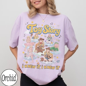 Może przedstawiać: Jasnofioletowy t-shirt z nadrukiem graficznym zawierającym tekst "Toy Story" oraz "i KNEW iT, i KNEW iT". Wz&oacute;r przedstawia wiele ilustrowanych postaci w strojach kowbojskich i kosmicznych siedzących na chmurach, otoczonych gwiazdami i nutami.