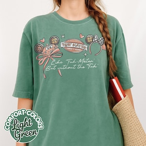 Puede incluir: Camiseta verde claro Comfort Colors con un gr&aacute;fico de Tow Mater de Cars. El dise&ntilde;o incluye un lazo rosa, ruedas de coche y el texto "Tow Mater Towing & Salvage" y "Like Tuh-Mater But without the Tuh."