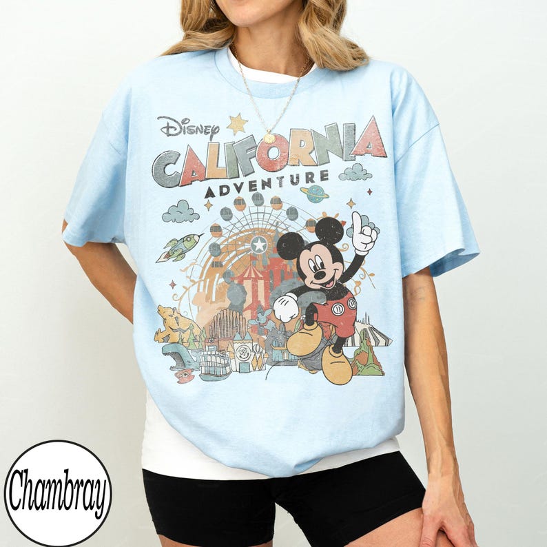 May include: Light blue t-shirt featuring a graphic of Mickey Mouse at California Adventure. The shirt has the text "Disney California Adventure" in a colorful design. The design includes a Ferris wheel, clouds, and other park elements.