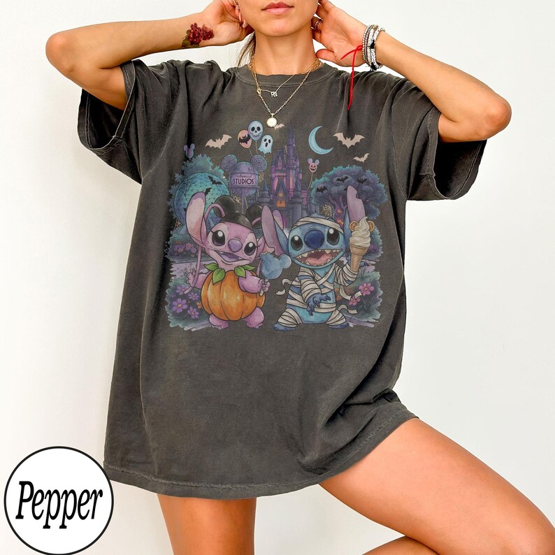 May include: A charcoal gray short-sleeve t-shirt featuring a graphic print of two blue alien characters in Halloween costumes. One character is dressed as a pumpkin, and the other is wrapped in bandages like a mummy, holding an ice cream cone.