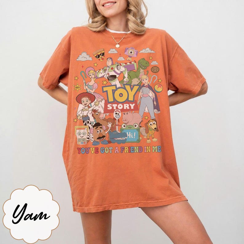 May include: An orange short-sleeve t-shirt featuring a colorful graphic print of Toy Story characters including Buzz Lightyear, Woody, and Jessie. The text reads TOY STORY and YOU'VE GOT A FRIEND IN ME. The design includes various small icons.
