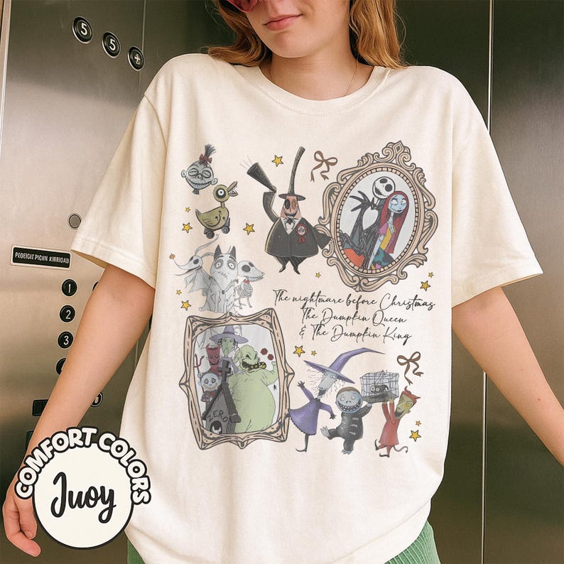 May include: A cream-coloured t-shirt featuring characters from "The Nightmare Before Christmas." The design includes framed portraits of Jack and Sally, and other characters. Text on the shirt reads "The nightmare before Christmas The Dampfia Queen & The Dampfia King."