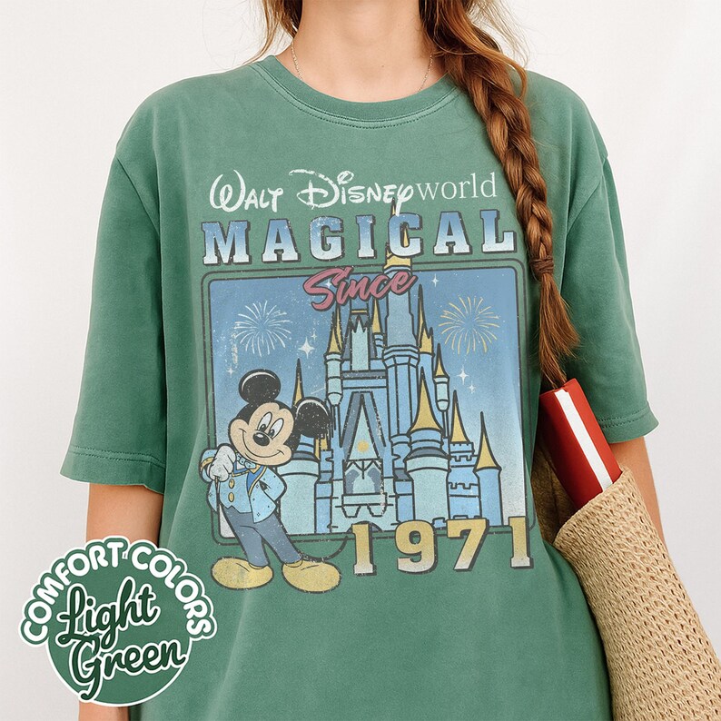 May include: Light green t-shirt with a graphic featuring Mickey Mouse in front of Cinderella's castle, with the text "Walt Disney World Magical Since 1971." The shirt also has the words "Comfort Colors Light Green."