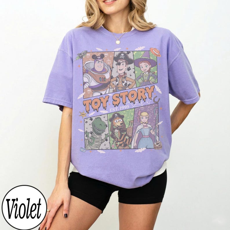 May include: A violet short-sleeve t-shirt featuring a graphic print of Toy Story characters in Halloween costumes. The text reads TOY STORY EST. 1995. The design includes Buzz Lightyear, Woody, Jessie, Rex, Slinky Dog, and Bo Peep in a grid layout.