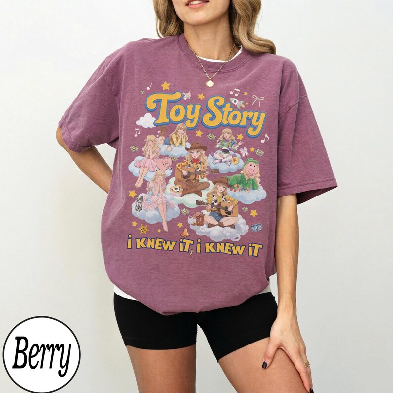 Może przedstawiać: Koszulka z kr&oacute;tkim rękawem w kolorze jagodowym z nadrukiem graficznym zawierającym tekst Toy Story oraz i KNEW IT, i KNEW IT. Wz&oacute;r przedstawia kilka ilustrowanych postaci z filmu siedzących na chmurach, otoczonych gwiazdami i nutami muzycznymi.