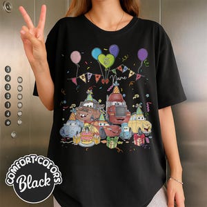 Peut inclure: T-shirt noir avec un graphisme color&eacute; de voitures de dessins anim&eacute;s, de ballons et d'une banni&egrave;re d'anniversaire. Le motif comprend le chiffre 5 et le mot "Name". Le t-shirt est de Comfort Colors.