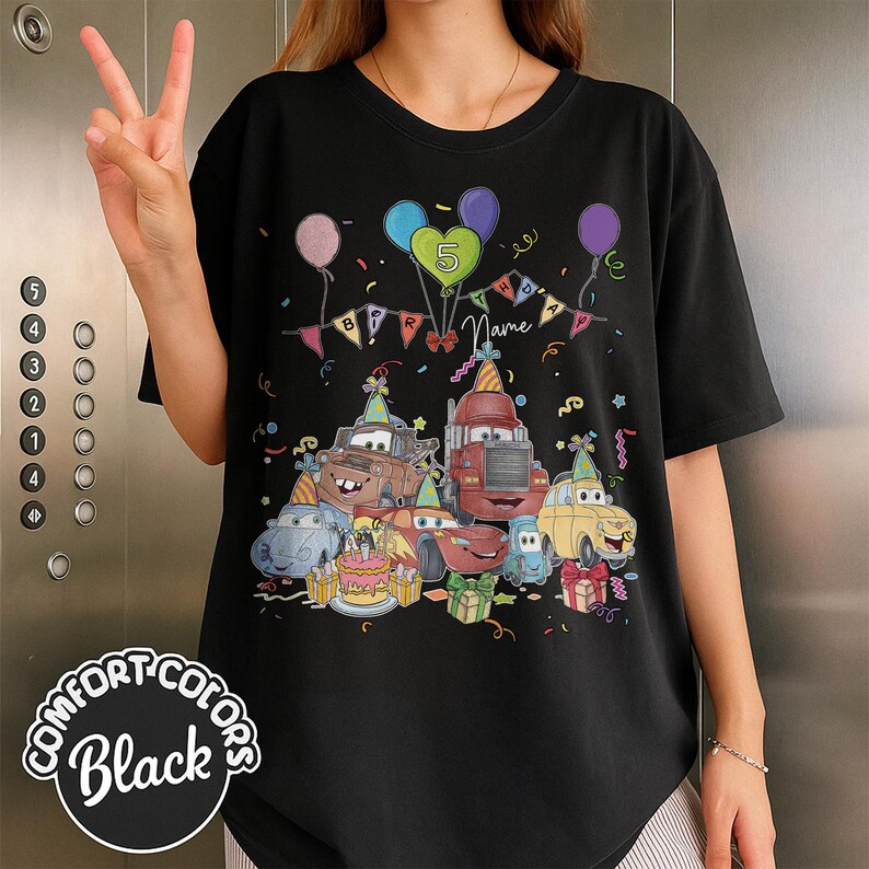 Peut inclure: T-shirt noir avec un graphisme color&eacute; de voitures de dessins anim&eacute;s, de ballons et d'une banni&egrave;re d'anniversaire. Le motif comprend le chiffre 5 et le mot "Name". Le t-shirt est de Comfort Colors.