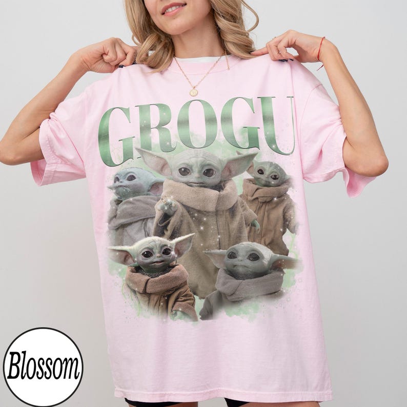 Puede incluir: Camiseta rosa claro con la palabra "GROGU" en verde y varias ilustraciones del personaje Grogu. La camiseta tiene mangas cortas y un corte holgado. El logo de Blossom est&aacute; en la esquina inferior izquierda.