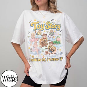 Może przedstawiać: Biały t-shirt z kr&oacute;tkim rękawem z nadrukiem graficznym zawierającym tekst Toy Story oraz I KNEW IT, I KNEW IT. Wz&oacute;r przedstawia liczne ilustrowane postacie, nuty, gwiazdki i chmury w kolorowej estetyce inspirowanej stylem retro.