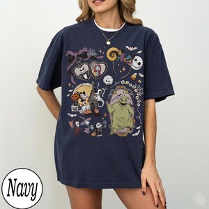 May include: Navy blue t-shirt featuring a colorful graphic of characters from a popular animated film. The design includes Jack Skellington, Sally, Oogie Boogie, and other spooky elements. The word "Navy" is printed on the bottom left.