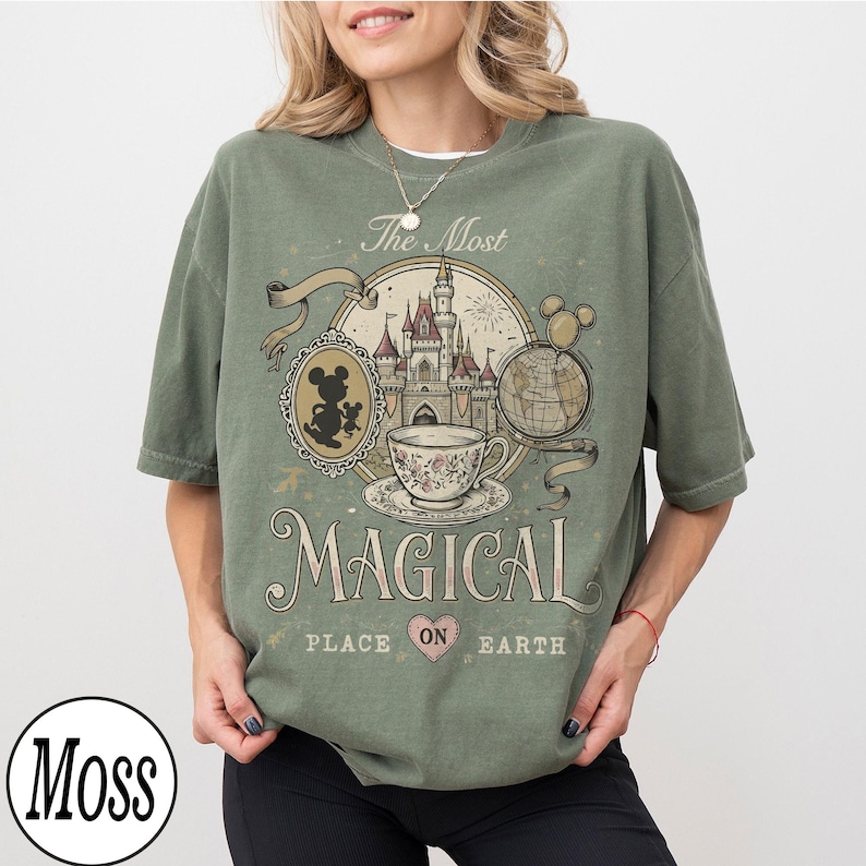 May include: Sage green t-shirt with a vintage-style graphic featuring a castle, teacup, and Mickey Mouse silhouette. The text reads "The Most Magical Place on Earth". The shirt has a relaxed fit.