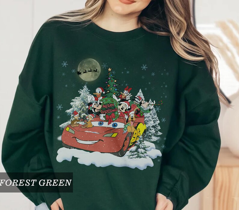 K&ouml;nnte beinhalten: Forstgr&uuml;nes Sweatshirt mit festlichem Aufdruck. Das Design zeigt ein rotes Auto mit Disney-Figuren, einen Weihnachtsbaum und den Text "Merry Christmas". Schneeflocken und ein Vollmond vervollst&auml;ndigen die Urlaubsszene.