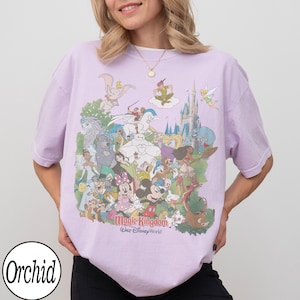 May include: A light purple t-shirt featuring a colorful graphic of various Disney characters, including Mickey Mouse, Dumbo, and Peter Pan. The text "Magic Kingdom Walt Disney World" is printed below the characters. The shirt has short sleeves and a crew neck.