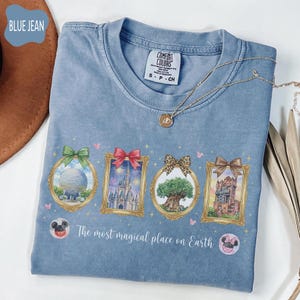 K&ouml;nnte beinhalten: Hellblaues Comfort Colors T-Shirt mit vier gerahmten Bildern von Themenpark-Wahrzeichen. Die Rahmen haben Schleifen in Gr&uuml;n, Rot, Leopardenmuster und Braun. Der Text "The most magical place on Earth" ist darunter gedruckt.