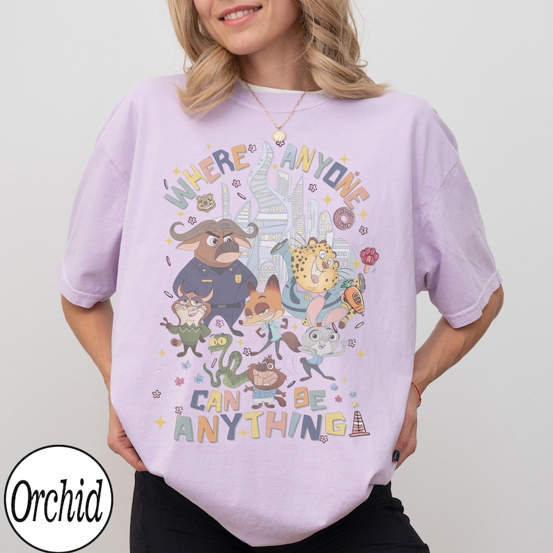 May include: A lilac t-shirt with a vibrant graphic of animated animal characters and the text "WHERE ANYONE CAN BE ANYTHING". The design includes a cityscape and various cartoon figures.