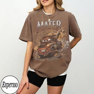 May include: Brown t-shirt featuring a cartoon image of Mater from the movie Cars, with the word "MATER" above the image. The graphic includes lightning bolts and a speedometer design. The shirt is a relaxed fit.