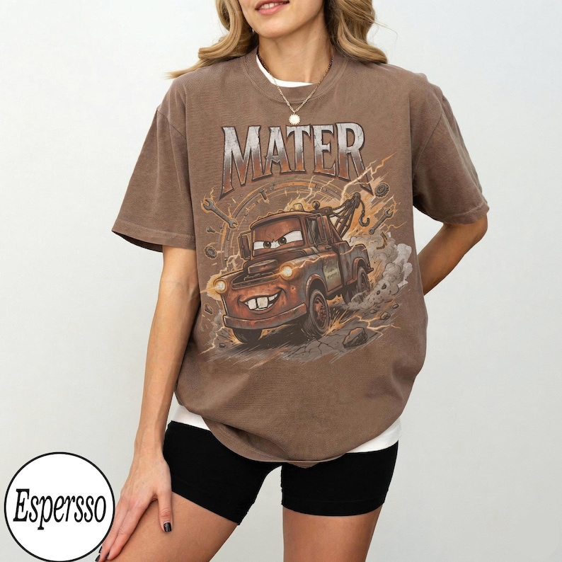 May include: Brown t-shirt featuring a cartoon image of Mater from the movie Cars, with the word "MATER" above the image. The graphic includes lightning bolts and a speedometer design. The shirt is a relaxed fit.