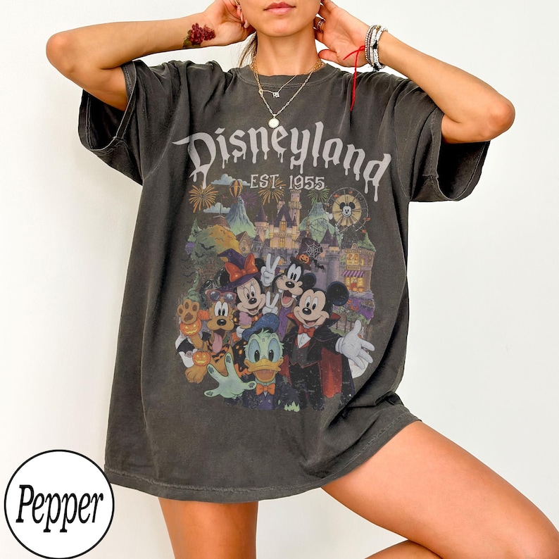 Puede incluir: Una camiseta de manga corta gris carb&oacute;n con un estampado gr&aacute;fico de personajes de Disney con disfraces de Halloween. El texto dice Disneyland EST. 1955. El dise&ntilde;o incluye a Mickey Mouse, Minnie Mouse, Donald Duck y Pluto en un castillo.