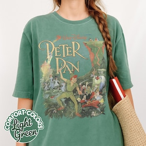 May include: Light green t-shirt featuring a vintage Peter Pan graphic. The design includes the title "Peter Pan" and illustrations of Peter Pan, Captain Hook, and other characters. The shirt also has the text "Comfort Colors Light Green".