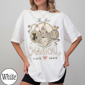 May include: White t-shirt with a colorful graphic design featuring a castle, teacup, and Mickey Mouse. The text reads "The Most Magical Place on Earth."