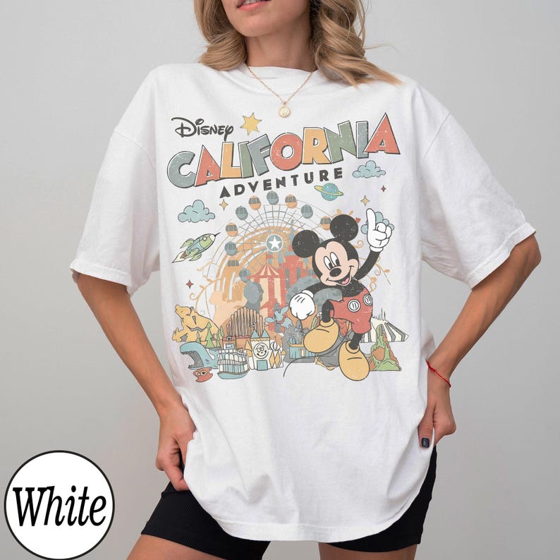 May include: White t-shirt featuring a colorful graphic of Mickey Mouse at California Adventure. The design includes the text "Disney CALIFORNIA ADVENTURE" with amusement park imagery. The shirt has short sleeves and a relaxed fit.
