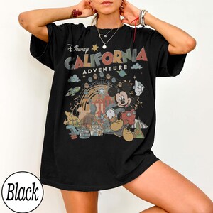 May include: Black t-shirt featuring a colorful graphic of Mickey Mouse at California Adventure. The design includes the text "Disney CALIFORNIA ADVENTURE" with a Ferris wheel, clouds, and other park elements. The shirt is a relaxed fit.