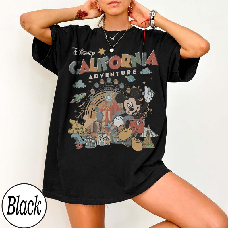 May include: Black t-shirt featuring a colorful graphic of Mickey Mouse at California Adventure. The design includes the text "Disney CALIFORNIA ADVENTURE" with a Ferris wheel, clouds, and other park elements. The shirt is a relaxed fit.