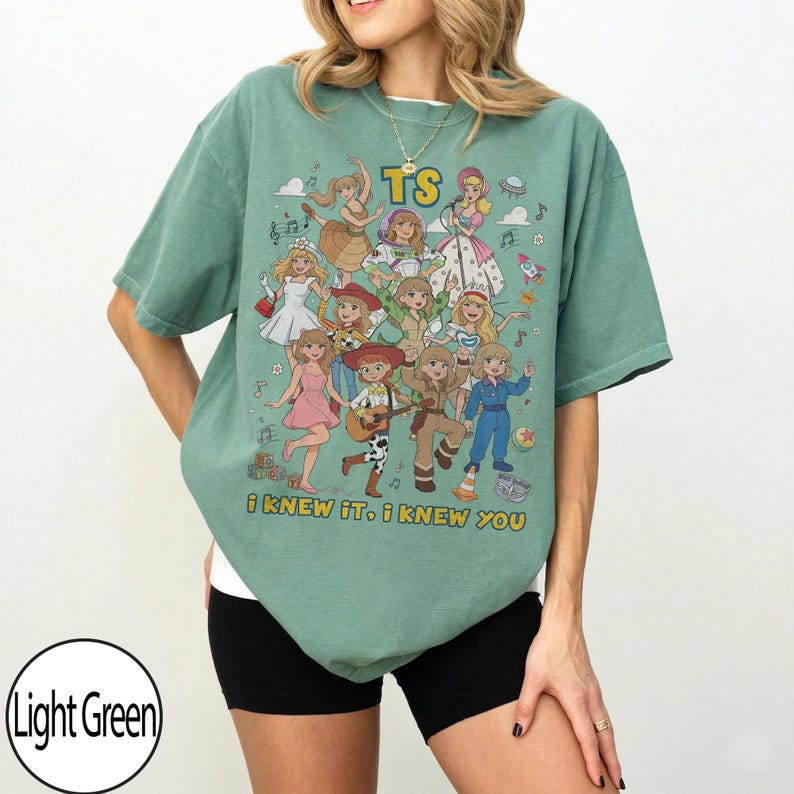 May include: A light green short-sleeve t-shirt featuring a graphic print of multiple cartoon characters in various outfits. The text "TS" appears at the top, and the text "i knew it, i knew you" is printed at the bottom of the graphic design.
