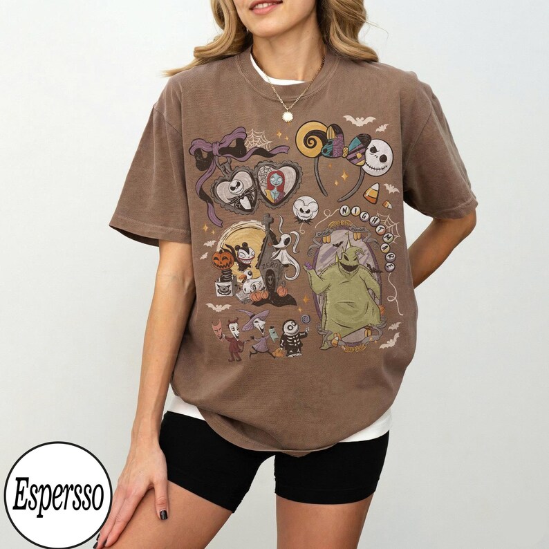 May include: Brown t-shirt featuring a colorful graphic of characters and elements from "The Nightmare Before Christmas." The design includes Jack Skellington, Sally, Oogie Boogie, and other iconic imagery. The shirt has a relaxed fit and short sleeves.
