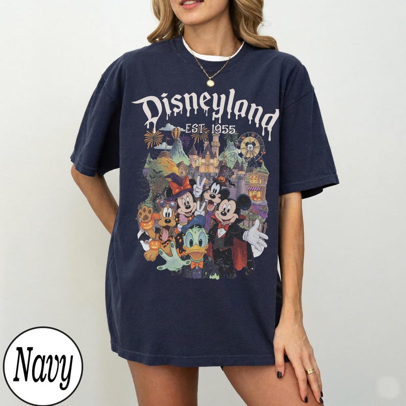 Puede incluir: Una camiseta azul marino de manga corta con un estampado gr&aacute;fico de personajes de Disney con disfraces de Halloween, incluyendo a Mickey Mouse, Minnie Mouse, Donald Duck y Pluto, con el texto Disneyland EST. 1955 y un castillo.