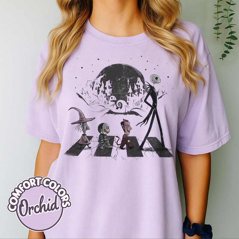 Peut inclure: T-shirt Comfort Colors lilas avec un motif de personnages traversant une rue, sur fond de pleine lune et de ville effrayante. Le t-shirt porte les mots "Comfort Colors Orchid" dans un cercle en bas &agrave; gauche.