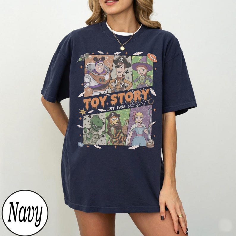 May include: A navy blue short-sleeve t-shirt featuring a graphic print of Toy Story characters in Halloween costumes. The design includes Buzz Lightyear, Woody, Jessie, Rex, Slinky Dog, and Bo Peep with the text Toy Story Est. 1995.