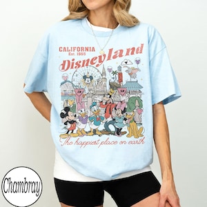 May include: Pale blue t-shirt with a Disneyland graphic featuring Mickey Mouse, Minnie Mouse, Donald Duck, Goofy, and Pluto. The graphic includes the text "California Est. 1955" and "The happiest place on earth."