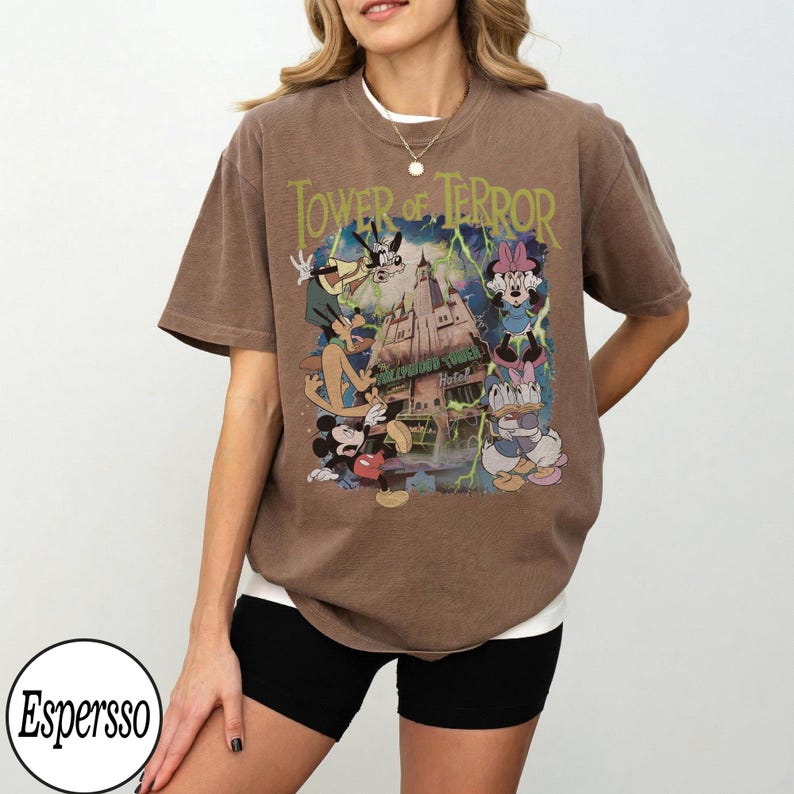 K&ouml;nnte beinhalten: Braunes T-Shirt mit einer Grafik von Disney-Figuren, darunter Micky Maus, Goofy und Minnie Maus, mit dem Text "Tower of Terror" und "Hollywood Tower Hotel". Das Shirt hat einen Vintage-Look.
