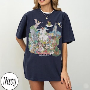 May include: Navy blue t-shirt featuring a colorful graphic of Disney characters, including Mickey Mouse, Cinderella, and Peter Pan, with the text "Magic Kingdom Walt Disney World". The shirt is a relaxed fit.