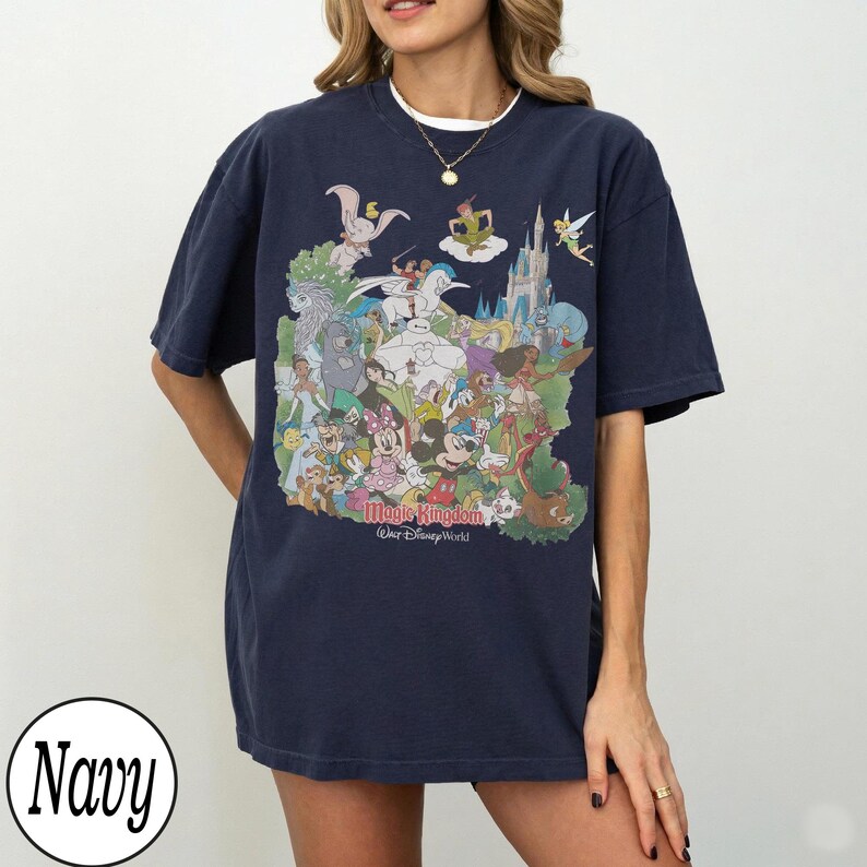 May include: Navy blue t-shirt featuring a colorful graphic of Disney characters, including Mickey Mouse, Cinderella, and Peter Pan, with the text "Magic Kingdom Walt Disney World". The shirt is a relaxed fit.