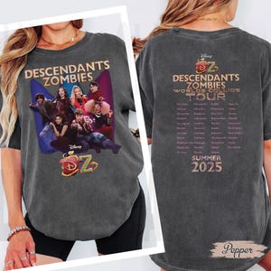 May include: Charcoal grey t-shirt with the text "Descendants Zombies" and a cast graphic. The back of the shirt shows "Worlds Collide Tour" and a list of cities, with "Summer 2025" at the bottom.