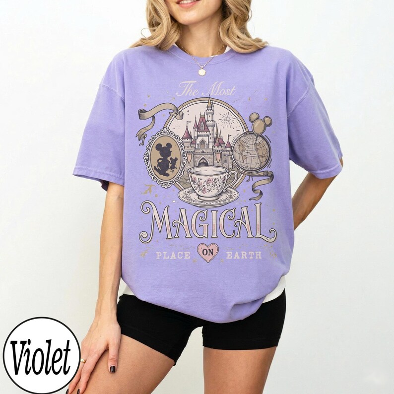 May include: A violet-colored t-shirt with a graphic design featuring a castle, teacup, and Mickey Mouse. The text on the shirt reads "The Most Magical Place on Earth."