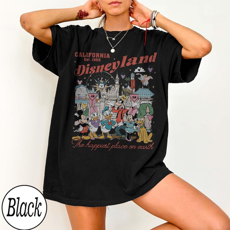 May include: Black t-shirt with a Disneyland graphic. The design features the text "CALIFORNIA Est. 1955 Disneyland" above a colourful illustration of Disney characters and landmarks. The phrase "The happiest place on earth" is below the illustration.