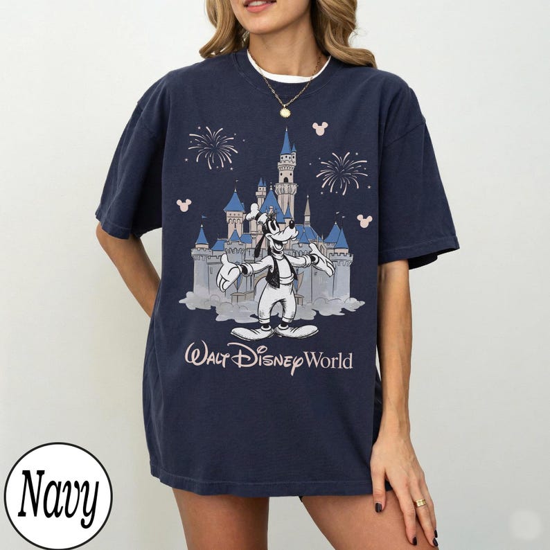 May include: Navy blue t-shirt with a graphic of Goofy in front of Cinderella's castle, fireworks, and Mickey Mouse icons. The text "Walt Disney World" is below the castle. The shirt has a relaxed fit.